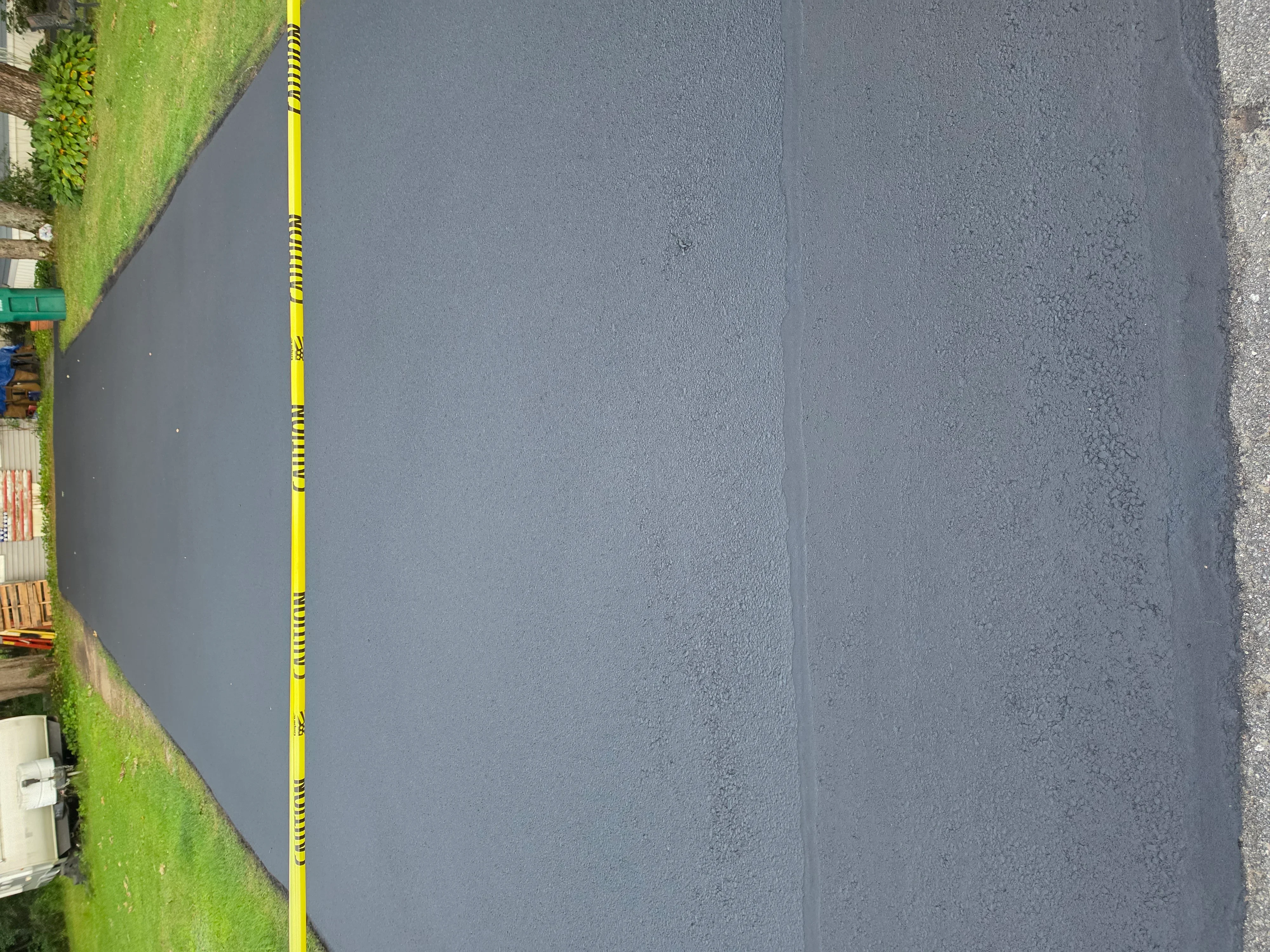 Freshly sealcoated asphalt driveway with dark gray finish and yellow measurement tape